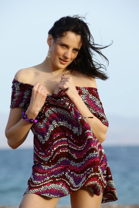 Brunette teen Sandra D gets naked on a pebbled beach while the wind blows