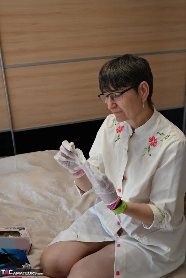 Amateur woman kneels on her bed while donning layers of latex gloves  - Short Hair, Mature, Glasses, Skirt, Clothed, Amateur, European, Brunette, Non Nude  - Photo 14