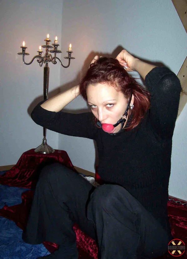 Clothed redhead affixes a ball gag while sitting afore a St Andrew's Cross  - Bondage, Clothed, BDSM, Non Nude  - Photo 4