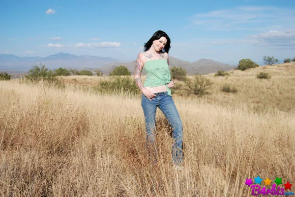 Tattooed brunette B4rbi3 undresses while standing in an expansive field  - Teen, Outdoor, Jeans, Tattoo, Undressing, Big Tits, Natural Tits, Skirt, Clothed, Ass  - Photo 1