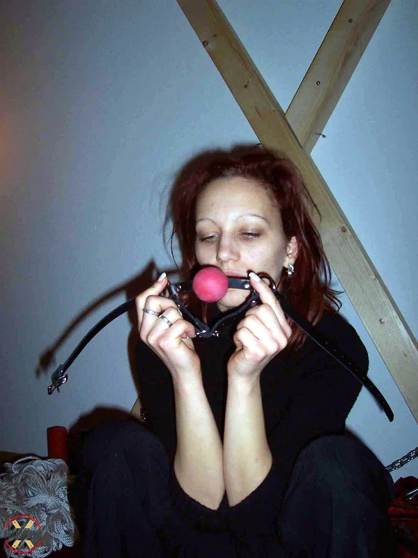 Clothed redhead affixes a ball gag while sitting afore a St Andrew's Cross  - Bondage, Clothed, BDSM, Non Nude  - Photo 1