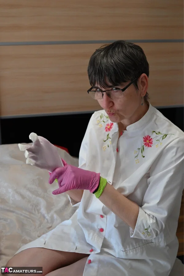 Amateur woman kneels on her bed while donning layers of latex gloves  - Short Hair, Mature, Glasses, Skirt, Clothed, Amateur, European, Brunette, Non Nude  - Photo 7