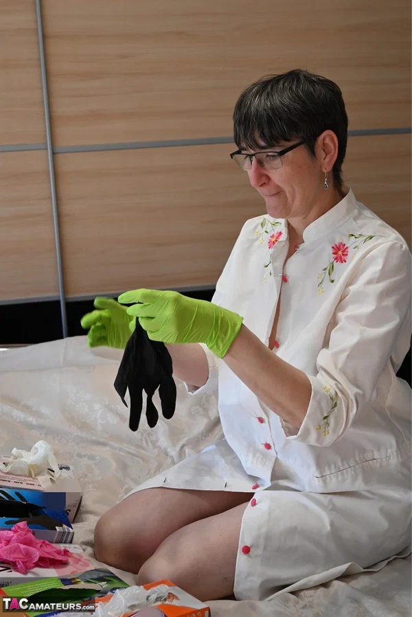 Amateur woman kneels on her bed while donning layers of latex gloves  - Short Hair, Mature, Glasses, Skirt, Clothed, Amateur, European, Brunette, Non Nude  - Photo 3