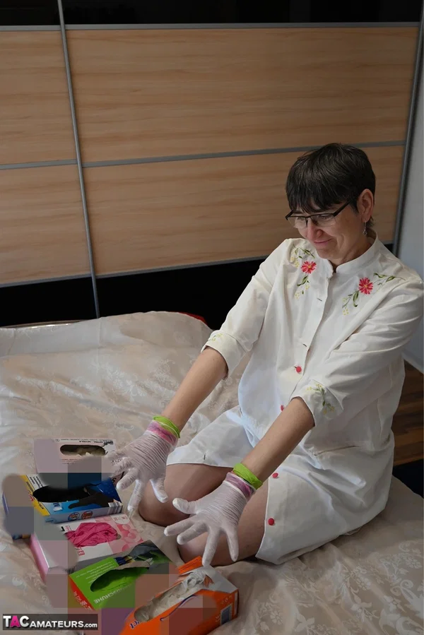 Amateur woman kneels on her bed while donning layers of latex gloves  - Short Hair, Mature, Glasses, Skirt, Clothed, Amateur, European, Brunette, Non Nude  - Photo 15