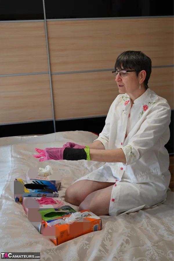 Amateur woman kneels on her bed while donning layers of latex gloves  - Short Hair, Mature, Glasses, Skirt, Clothed, Amateur, European, Brunette, Non Nude  - Photo 5