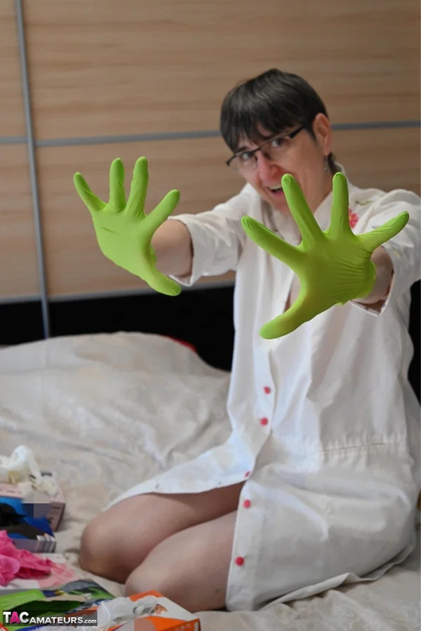 Amateur woman kneels on her bed while donning layers of latex gloves  - Short Hair, Mature, Glasses, Skirt, Clothed, Amateur, European, Brunette, Non Nude  - Photo 2