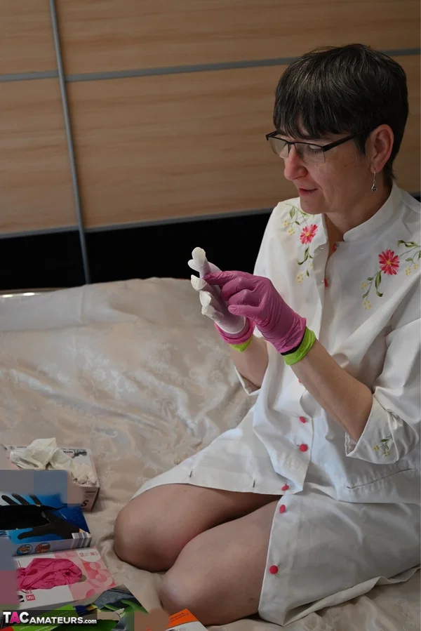 Amateur woman kneels on her bed while donning layers of latex gloves  - Short Hair, Mature, Glasses, Skirt, Clothed, Amateur, European, Brunette, Non Nude  - Photo 8